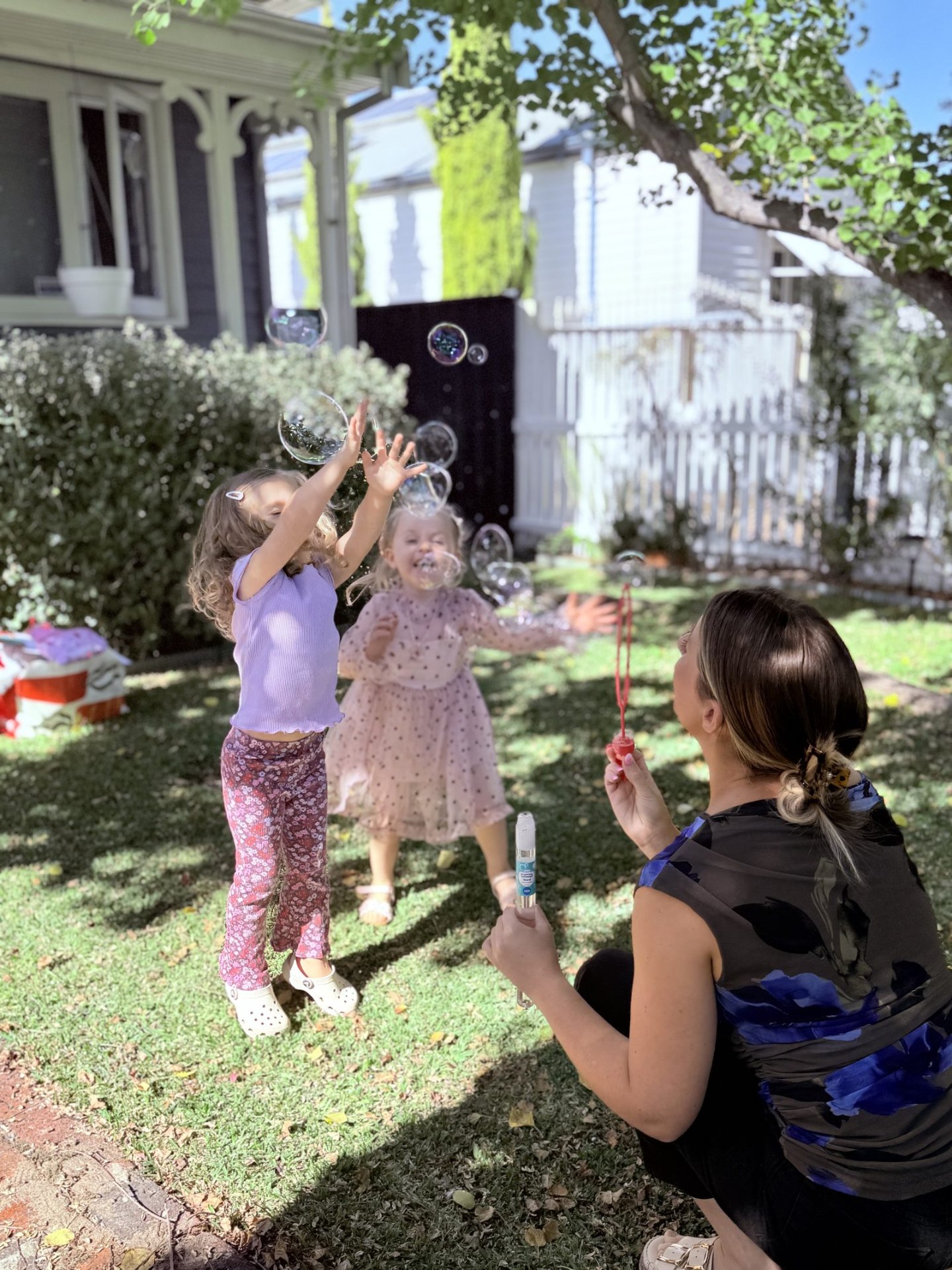 Speech pathologist Lara blowing bubbles in the garden as two delighted children reach to catch them