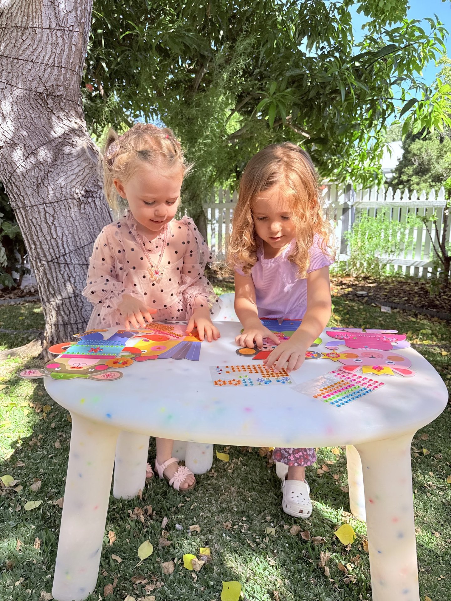 Two children working on a sticker activity together at an outdoor table