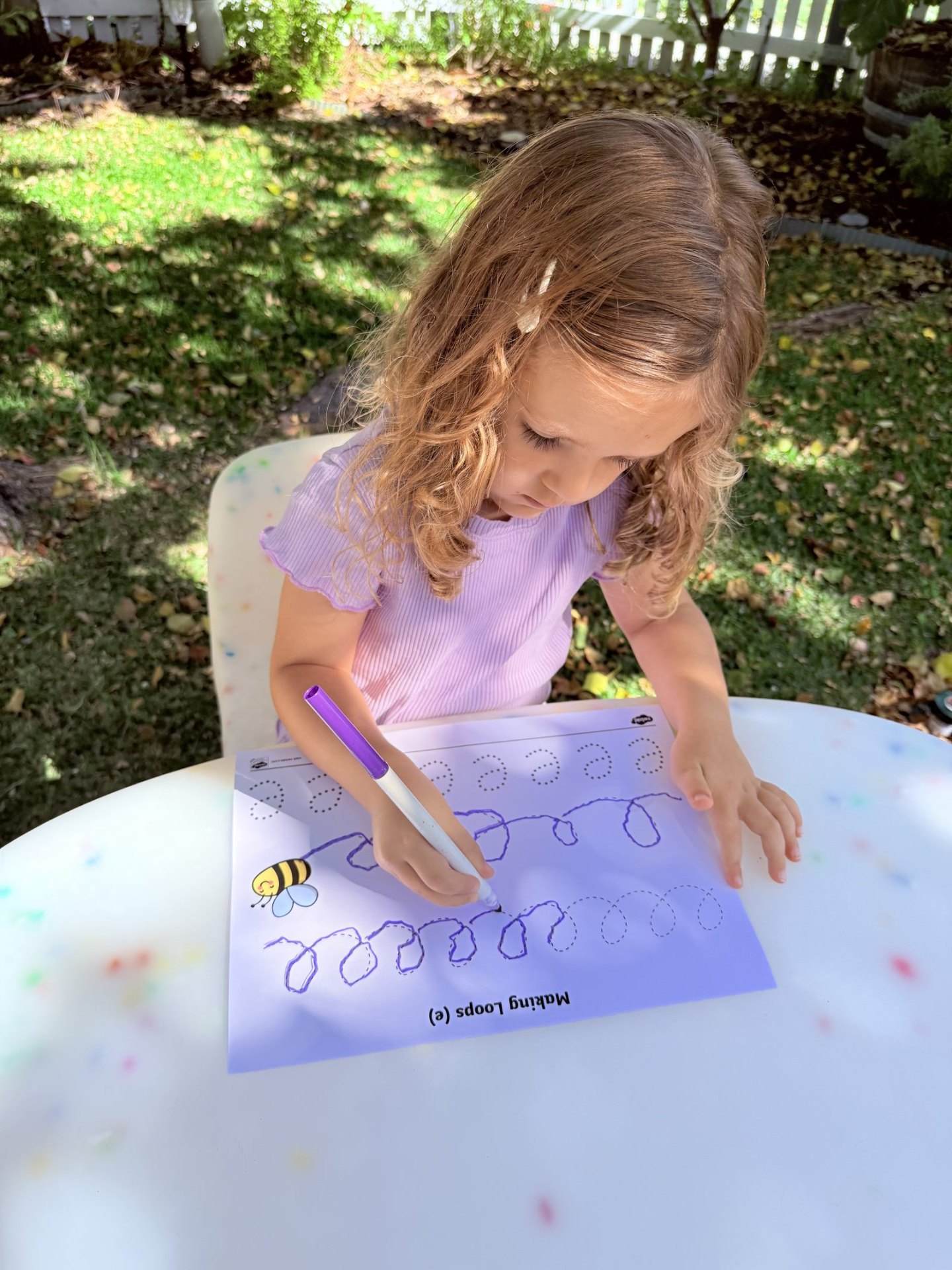 Young child practising letter formation with a worksheet outdoors